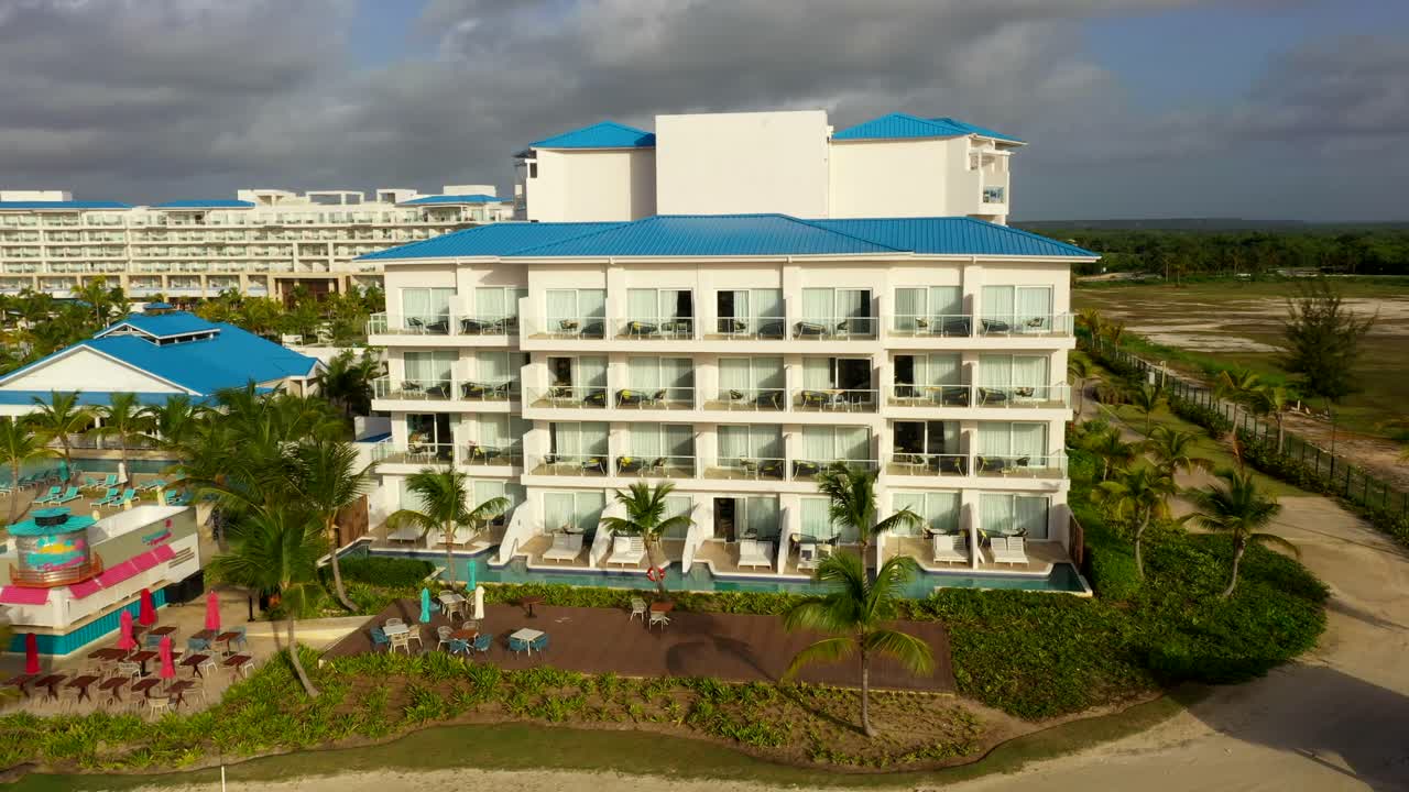 Aerial orbit of white beachfront hotel surrounded by greenery and palm trees in Cap Cana, DR
