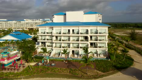 aerial orbit of white beachfront hotel surrounded by greenery and palm trees in cap cana, dr