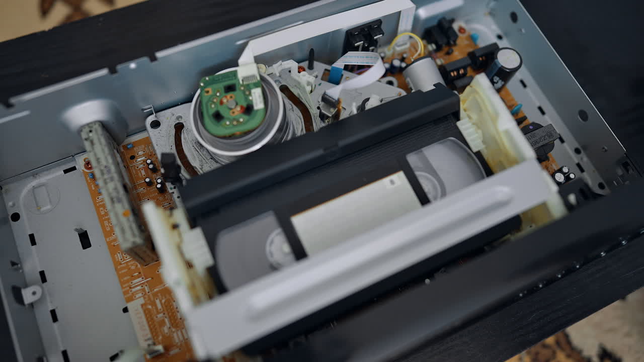 Opened lid of the VHS player. Tape enters the device and reels starts moving. Close up