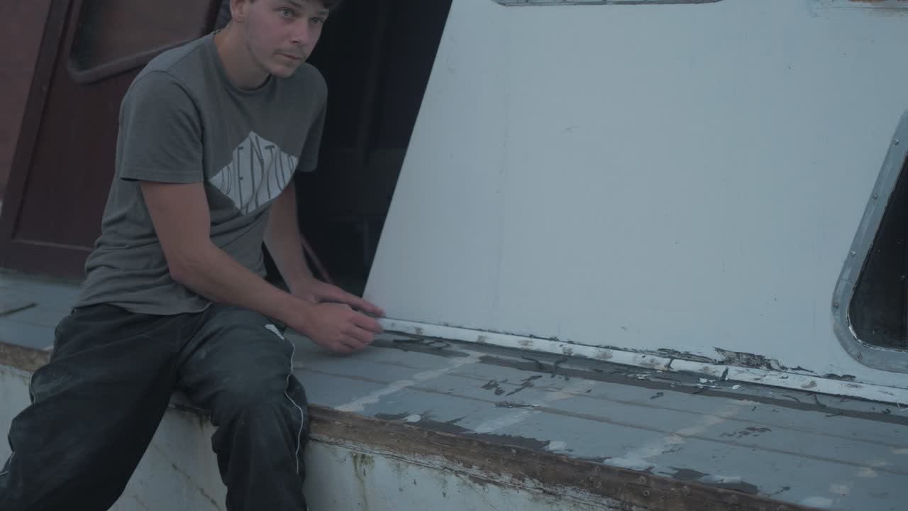 Young caucasian carpenter trimming excess sikaflex sealant on wooden boat trim