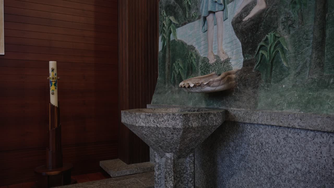 Stone baptismal font with candle and mural inside a modern church