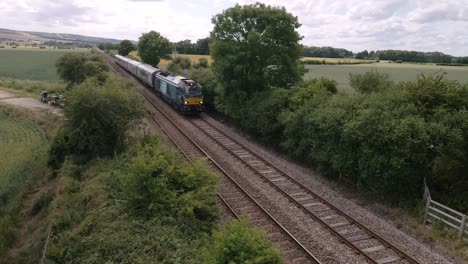 vista aérea de ángulo bajo de un tren de pasajeros que conduce por vías en el campo en inglaterra