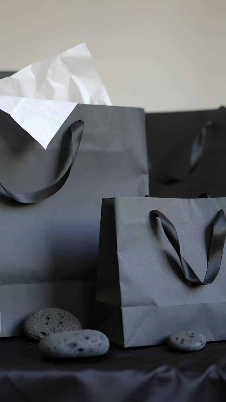 Vertical video: Zooming camera centering black bags, tissue, gift, stones on tabletop for contrast
