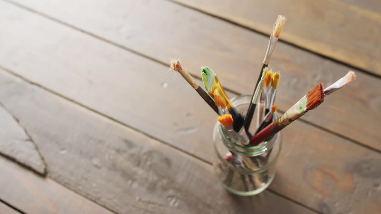 video de ángulo alto de pinceles de pintura de pie en un frasco en tablas de madera con espacio de copia