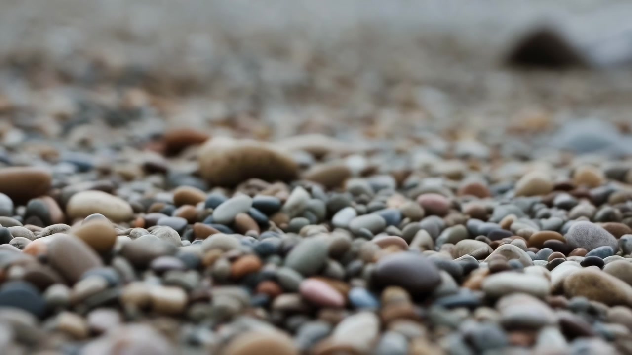 Seixos em uma praia, sem ação observada, com areia, em close-up ao nível do solo, com tons de cinza e marrom, e um clima calmo e sereno, com objetos próximos