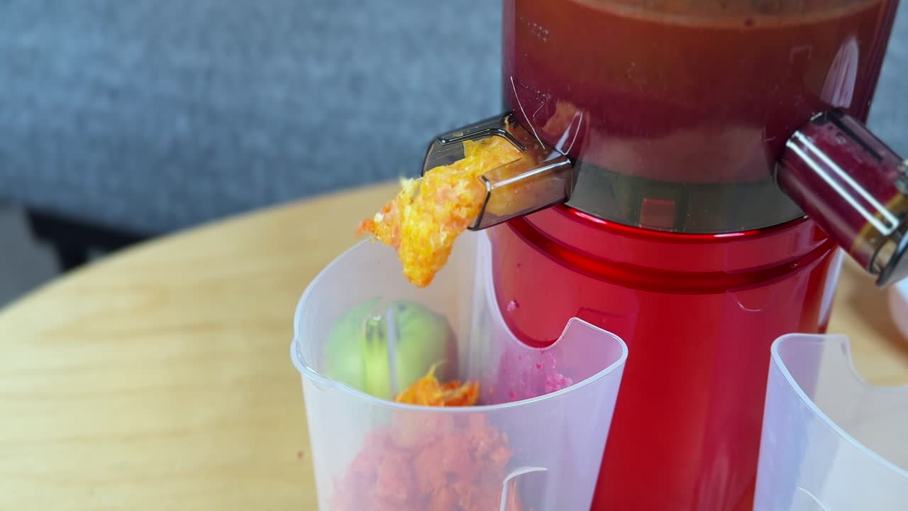 4K close-up of a slow juicer extracting fresh fruit pulp into a container. Vibrant colors, smooth kitchen operation, and clean indoor setting ideal for health, food, and lifestyle content