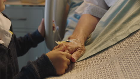 little boy holding grandmothers hand granny lying in hospital bed child showing affection at bedside for grandparent recovering from illness health care family support