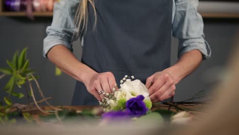 Vista-De-Cerca-De-Las-Manos-De-Una-Asistente-De-Fotografía-De-Flores-Atando-Un-Ramo-De-Flores-Sobre-Su-Mesa-Con-La-Cinta.-Tiro-En-Cámara-Lenta