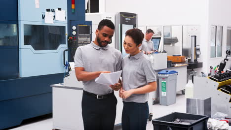 Engineer-And-Apprentice-Discuss-Plans-On-Floor-Of-Engineering-Workshop