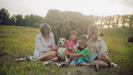 smiling family sitting on grass near hay bale, enjoying outdoor bonding while petting a friendly dog, warm golden sunlight enhances joyful atmosphere