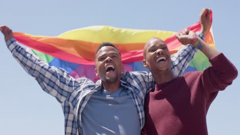 feliz pareja de hombres homosexuales afroamericanos que sostienen la bandera del arco iris lgbt, cámara lenta