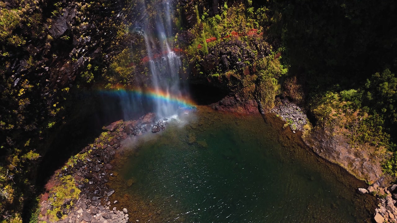 Aerial view of waterfall creating rainbow over natural pool in Madeira