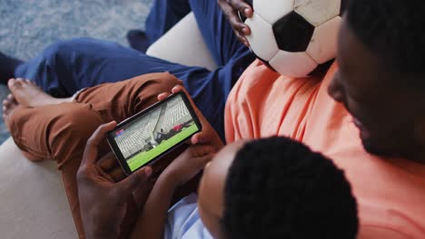 composite of father and son at home watching rugby match on smartphone