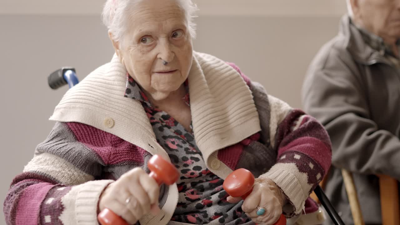 Vecchia donna che si esercita con i manubri seduta in una casa di riposo