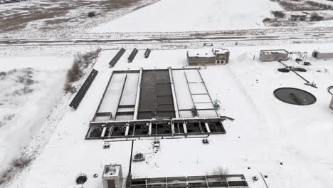 Drone-Sobrevuela-La-Planta-De-Tratamiento-De-Agua-Ubicada-En-Pequeños-Pueblos-En-Invierno,-Paisaje-Cubierto-De-Nieve