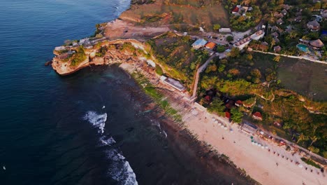 drone footage captures balangan beach in bali at sunset showing dramatic cliffs overlooking the ocean as gentle waves roll across the sandy shoreline creating a stunning tropical scene