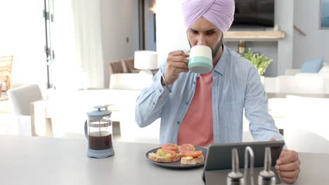 drinking coffee, man in turban using tablet while having breakfast at home