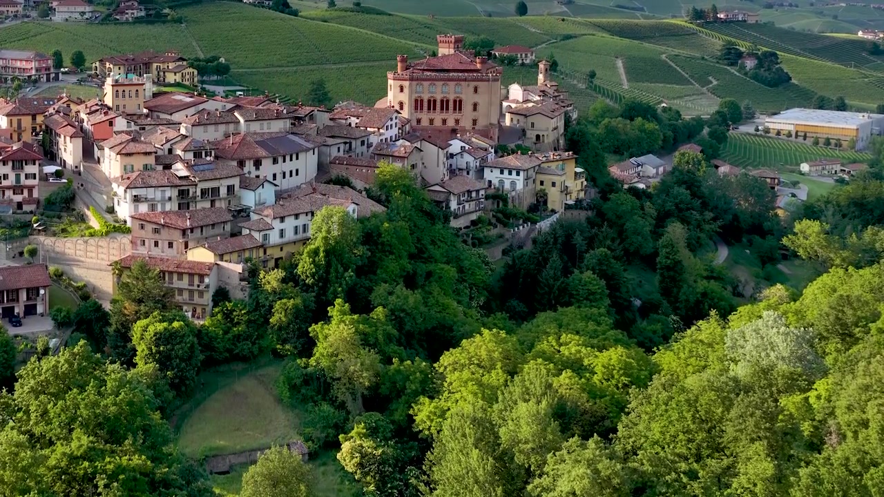 Panoramica con drone sul villaggio e il castello di Barolo, circondati da rigogliosi vigneti verdi e colline.