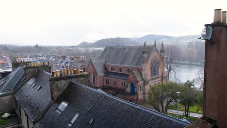 Scenic-aerial-view-of-houses,-church-and-rooftops-with-a-glimpse-of-the-River-Ness-on-a-wet-raining-day-in-Inverness-city,-Scotland-UK