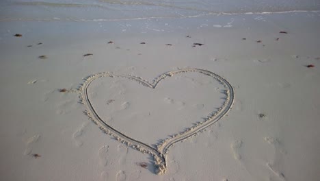 medium tight static shot of heart with an arrow through it on a beach with water lapping on the sand