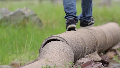 Young-man,-wearing-jeans-and-sneakers,-walks-along-pipe-and-jumps-off-into-field