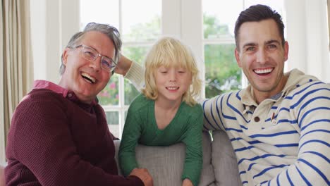 video portrait of happy caucasian father, grandfather and grandson sitting on couch smiling