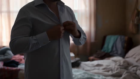man buttoning his shirt in a bedroom