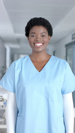 vertical video of portrait of happy african american female doctor wearing scrubs, slow motion