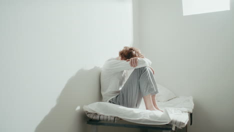 Sad Patient Sitting Alone on Bed in Room at Psychiatric Hospital