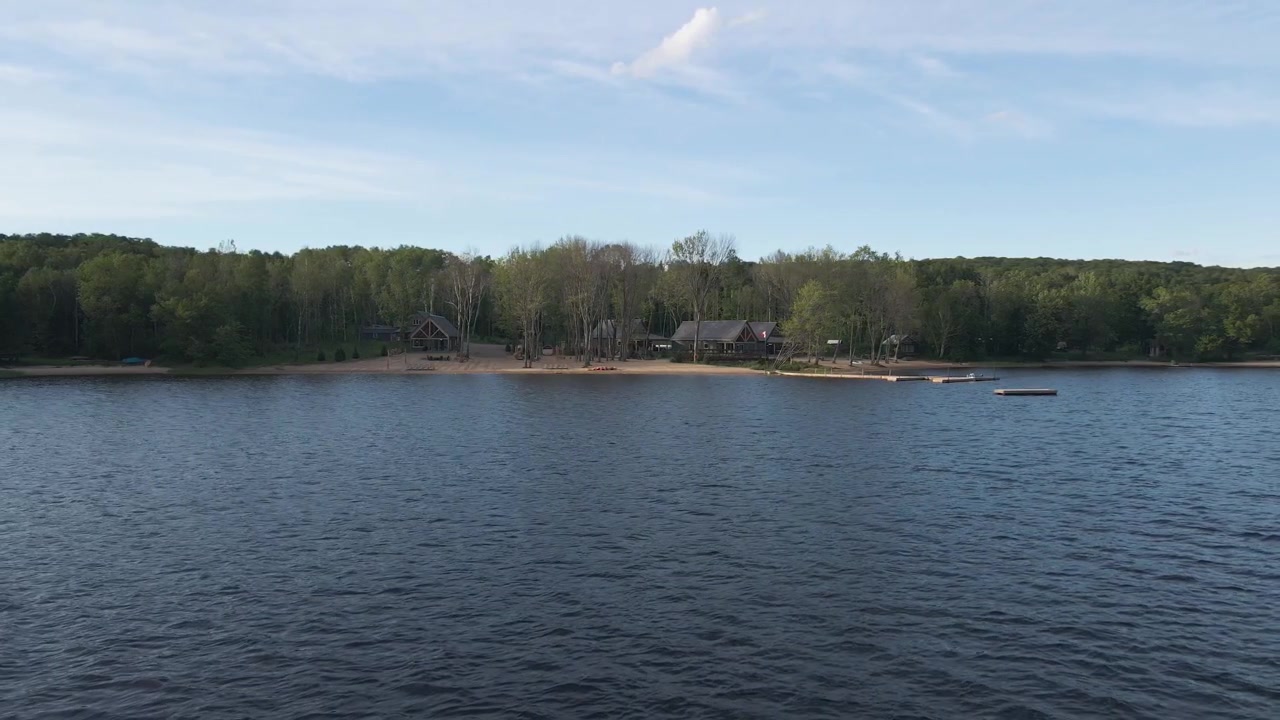 Hytter ved søen og sandstrand ved Commanda-søen i Restoule, Ontario, drone sporer mod venstre under en tyndskyet himmel.