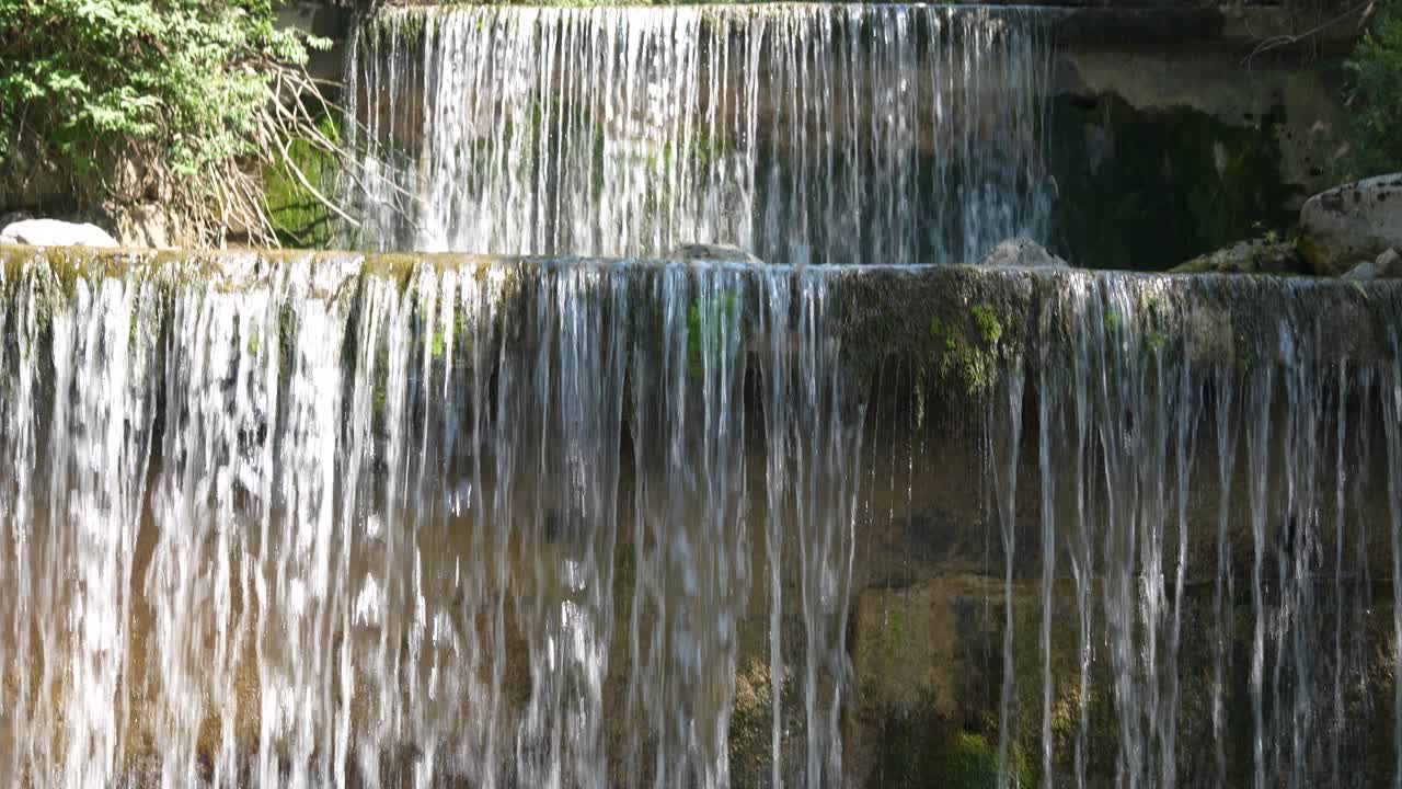 Close up of water streams cascading over moss-covered rock wall into clear pool in Swiss nature