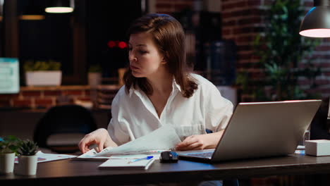 Worker-looking-over-paperwork-containing-financial-graphs,-researching-data