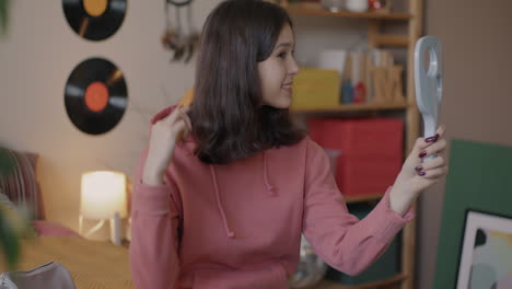 teenage girl checking her hair in front of a mirror in her bedroom
