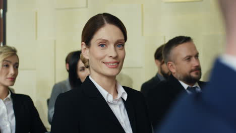 caucasian young businesswoman sitting on a empty chair among people in a conference room, then she turns her face to the camera and smiling