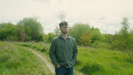 man stands on grassy hill in front of cloudy sky, surrounded by lush open countryside, staring out
