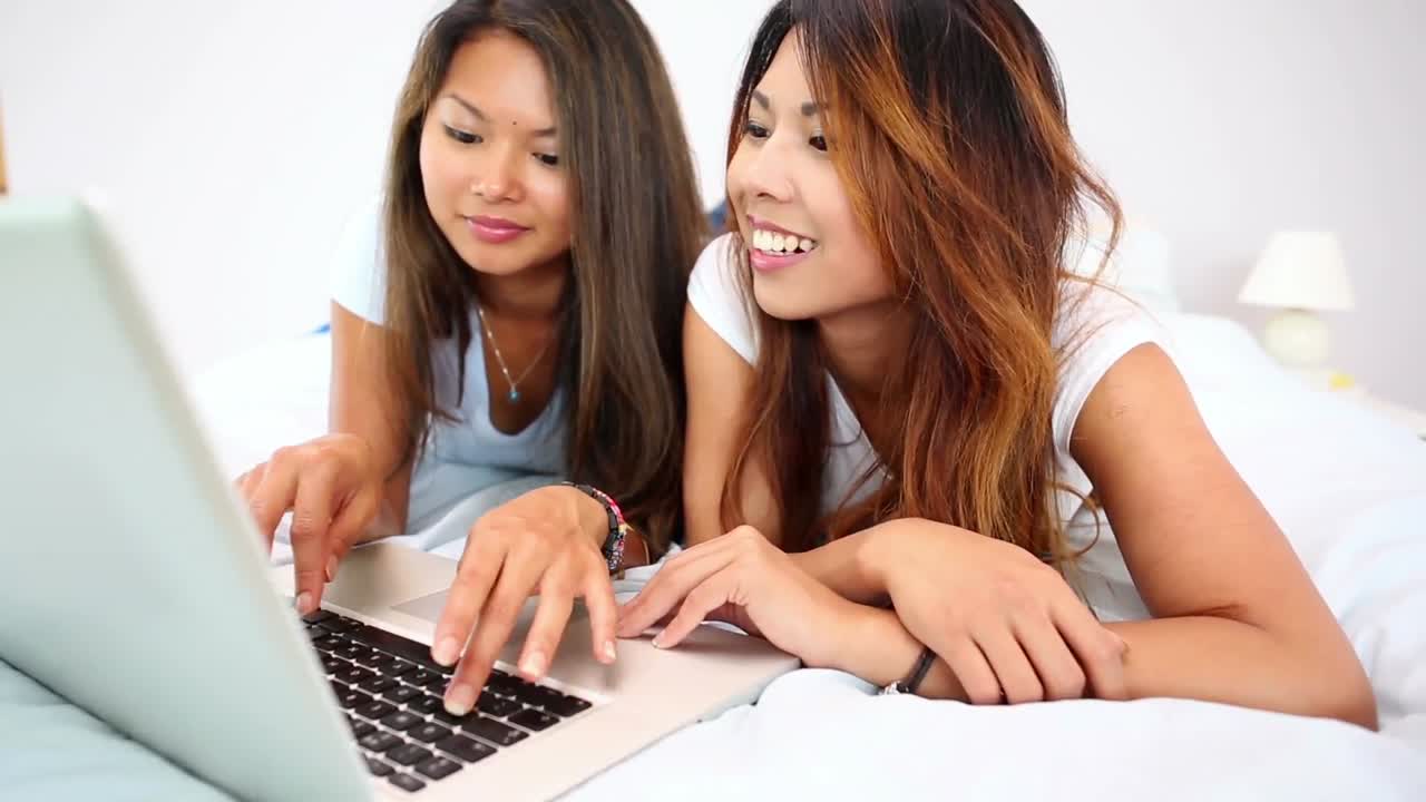 노트북을 이용해 침대에 누워 있는 예쁜 행복한 자매들