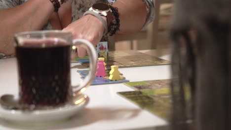 Detail-of-board-game-and-cup-of-tea-on-table,-moving-characters-by-hand
