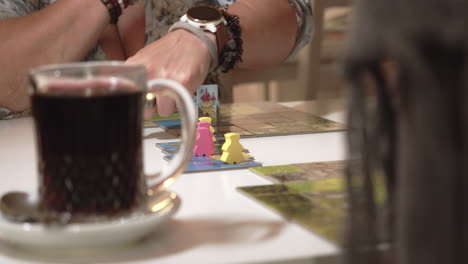 detail of board game and cup of tea on table, moving characters by hand