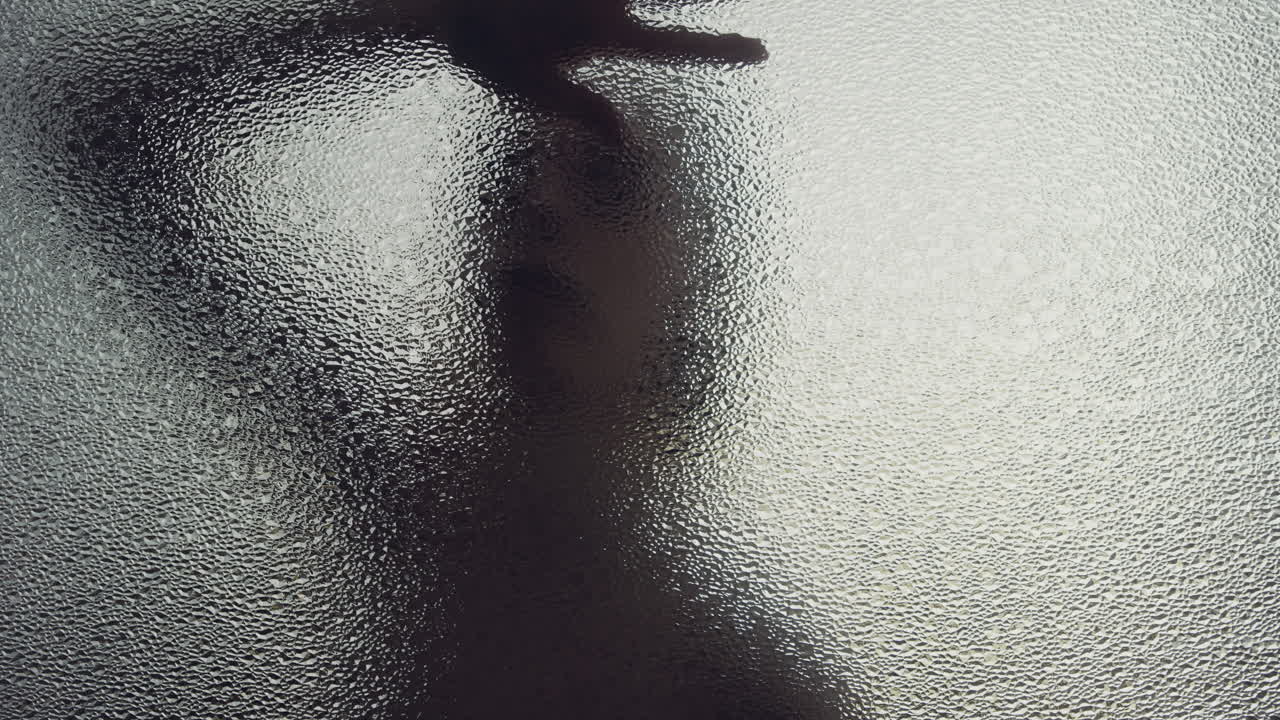A female silhouette behind the frosted window touches the glass slowly