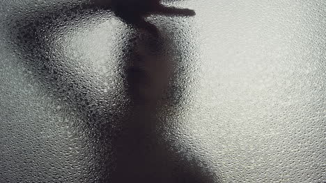 a female silhouette behind the frosted window touches the glass slowly