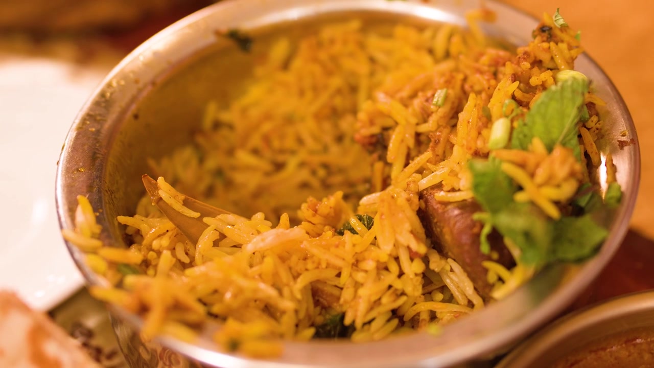 Primer plano de una cuchara levantando arroz basmati aromático y pollo de un cuenco metálico.