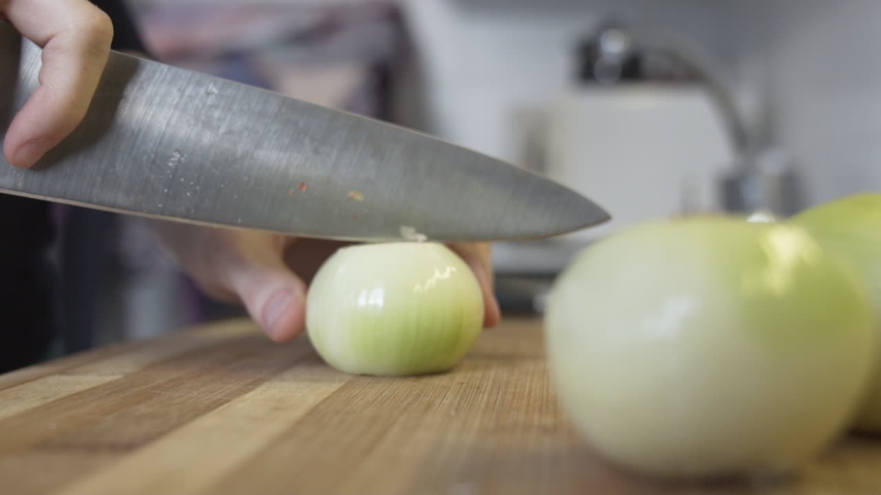 Slow-motion shot as taking an onion to the chopping board and cutting it in half, slicing it in the kitchen, raw ingredient