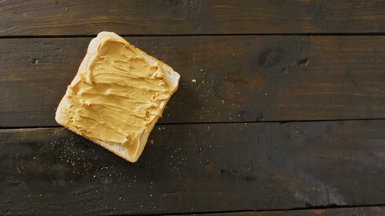 Video of close up of toast with peanut butter on wooden background