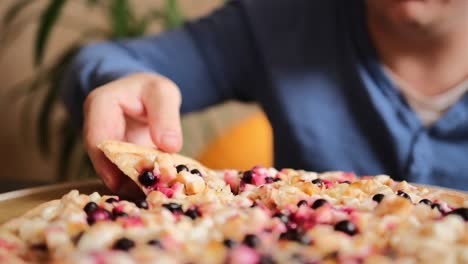 the guy takes a slice of sweet pizza. large round sweet pizza pie with apple pieces, berries, almond slices and condensed milk.