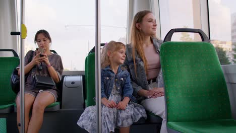 Family-rides-in-public-transport,-woman-with-little-child-girl-sit-together-and-look-out-window-tram