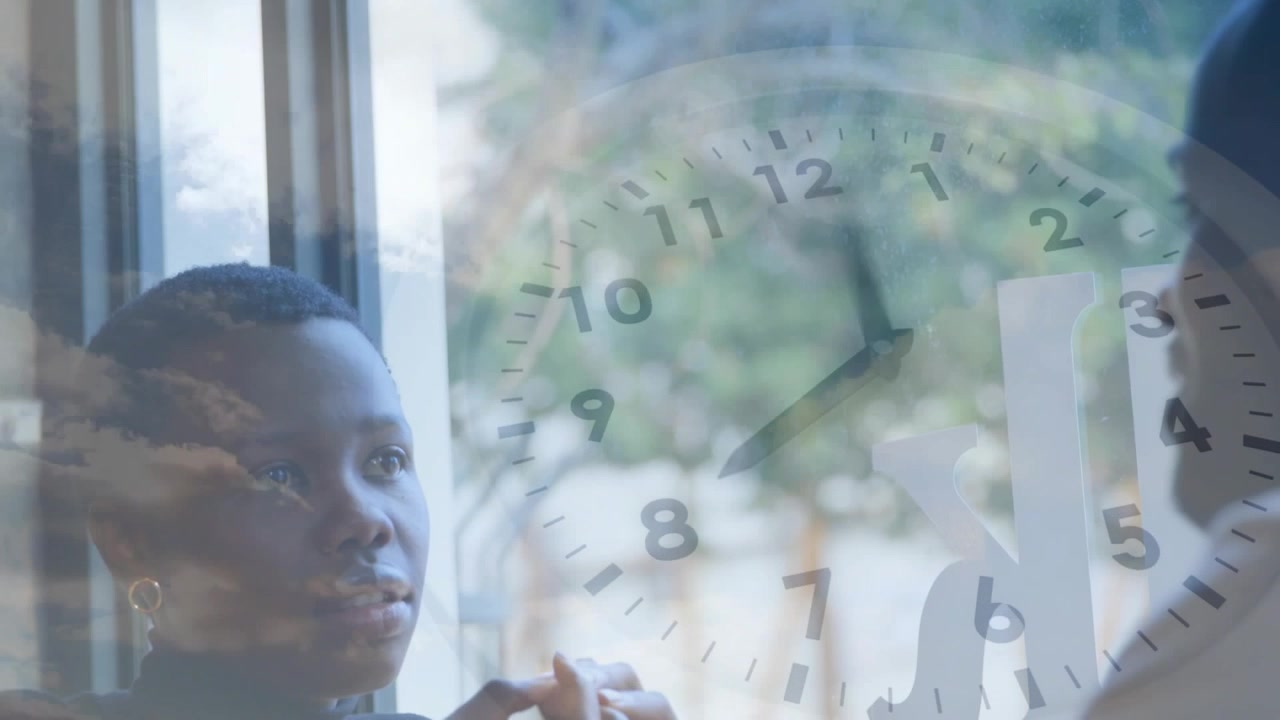 Woman sitting by window in therapy, responding to man speaking, fiddling rings under clock overlay