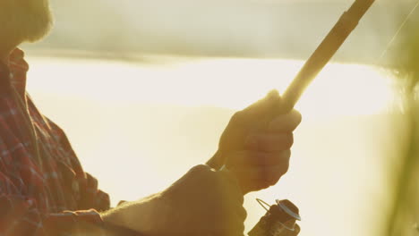 close-up view of caucasian senior man rolling the line of the fishing rod on a cloudy morning