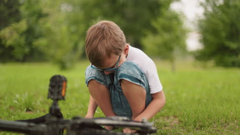 a young boy squats close to his fallen bicycle, facing down in deep thought