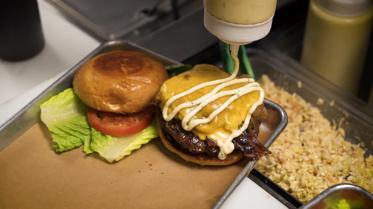 셰프가 치즈버거 위에 특별한 소스를 뿌리고, 요리사가 버거 드레싱을 마무리하고, 슬로우 모션 4k