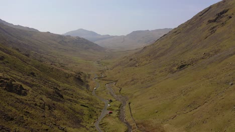 Wrynose-Pass-in-The-Lake-District-drone-fly-by-shot-above-a-road-in-between-two-sides-of-a-mountain